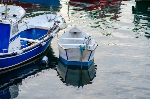 Huzurlu bir balıkçı teknesinin ve huzurlu bir limana bağlı beyaz bir kayığın sabah manzarası, su yüzeyine yansıyor, rahatlama ve kıyı yaşamını çağrıştırıyor..