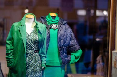Bir şehir butiğinde mankenler üzerinde moda yeşil kıyafetlerin sergilenmesi, mevsimlik eğilimleri vurgulamak ve kentsel alışveriş yapanlar için yaratıcı vitrin süsleri.