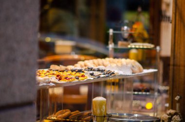 Fırının içini renkli hamur işleri ve kurabiyelerle camdan bir rafa davet etmek sıcak ve misafirperver bir ortam yaratır. Gıda pazarlaması ya da cafe görselleri için ideal.