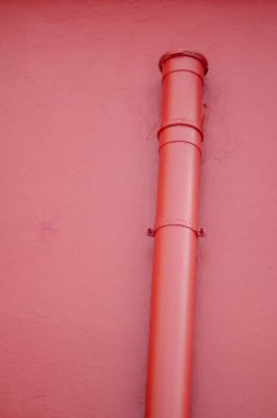 Pembe boyalı bir duvara bağlı dikey kırmızı metal bir boru bulunan minimalist fotoğraf, kent tasarımı, inşaatı veya mimari projelerde kullanılmak için mükemmel.