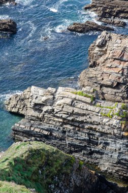 Açık mavi denize bakan desenli taş katmanlı dramatik kayalık kıyı şeridi, doğal erozyon, ham jeoloji ve manzaralı açık hava manzarası.