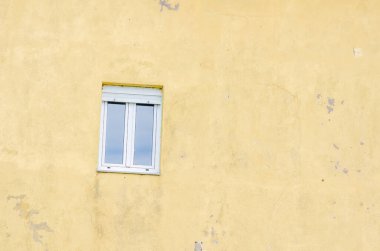 Yıpranmış bir konutun minimalist dış görüntüsü, kentin cazibesi ve kopyası için yeri olan dokulu sarı bir duvarın klasik beyaz penceresi..