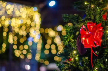 Parlak kırmızı kurdeleli süslü bir Noel ağacına yakın çekim yapmak sıcak, şenlikli bir atmosfer yaratır. Mevsimsel kutlamalar için mükemmel olur..