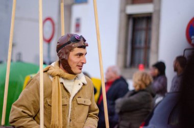 Deri kasklı, gözlüklü ve eşarplı klasik bir pilot gibi giyinmiş bir adam canlı bir halk festivalinin tadını çıkarıyor. Nostalji, eski moda ve havacılık tarihi konuları için mükemmel..