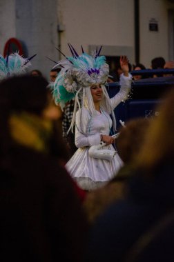 Şenlikli atmosferde kutlama yapan, tüylü başlıklı, gülümseyen bir sanatçıyla canlı bir sokak geçit töreni sahnesi. Kutlama, sokak festivali ve eğlence için mükemmel bir tema..