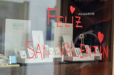 Sevgililer Günü için süslenmiş romantik mücevher mağazası zarif kolyeler ve yüzüklerle, pencerede el boyaması bir 'Feliz San Valentin' karşılaması.