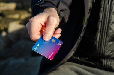 Dışarıda Revolut Visa kartı tutan kişi, kolay mobil bankacılığı, Avrupa 'da güvenli irtibatsız ödemeleri ve modern yaşam tarzını sembolize ediyor.