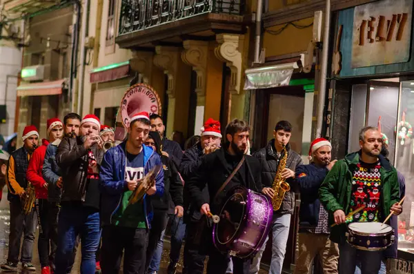 Bir grup müzisyen, bir Noel geçidi boyunca canlı bir gösteri yaparak, dekore edilmiş bir şehir merkezinde bayram neşesi ve şenlik havası yayıyor..