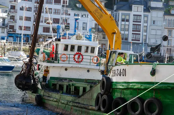 Büyük bir kazıcıyla donatılmış bir tarama gemisi hareketli bir limanda çalışır, rıhtımdaki su yolunu temizler ve renkli kentsel binalar, endüstriyel faaliyet.