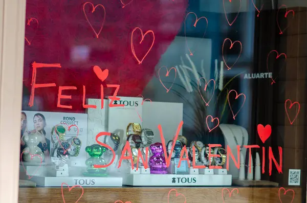 Sevgililer Günü için süslenmiş butik bir pencerede sergilenen renkli mücevherler ve saatler, el yazısıyla selamlama ve kalp motifleriyle romantik bir kutlama havası yaratıyor..
