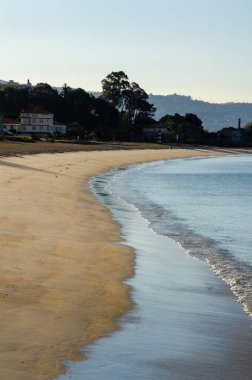 Sakin bir kumsalda sakin bir sabah sahnesi, sakin bir deniz, arka planda sakin bir sahil kasabası, rahatlamak ya da seyahat için mükemmel bir ilham kaynağı..