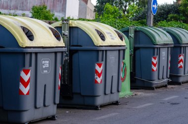 Şehir caddesi boyunca renklendirilmiş kapaklı büyük geri dönüşüm kapları atık ayrımını ve sürdürülebilir şehir yaşamını destekliyor. Temiz çevre ve sağlık hizmetleri.