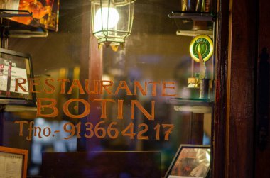 İspanya 'nın Madrid kentindeki Botin Restoranı' nın sıcacık penceresi samimi ve davetkar bir atmosferi gösteriyor. Cam tabela tarihi cazibeyi ve yerel gastronomiyi yansıtıyor..
