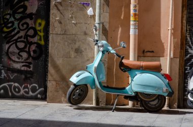 Kahverengi deri koltuklu klasik retro scooter. Güneşli bir Avrupa şehir sokağında dokulu bir duvar ve grafiti duruyor. Retro cazibe ve canlı şehir yaşamını çağrıştırıyor..