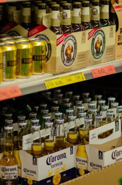 Çeşitli uluslararası bira markaları süpermarket raflarında sergileniyor, görünür fiyat etiketleriyle perakende satış ortamında şişeler ve tenekeler sergileniyor.