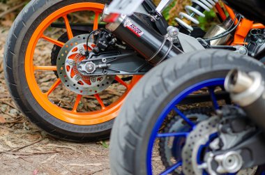 Renkli jantları ve disk frenleri olan, orman yolunda park edilmiş modern spor motosiklet tekerleklerinin detaylı yakın çekimi. Hız, güç ya da motosiklet mühendisliği için mükemmel..