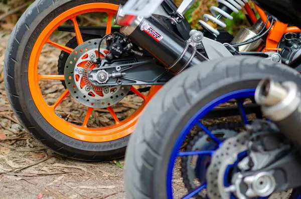 Renkli jantları ve disk frenleri olan, orman yolunda park edilmiş modern spor motosiklet tekerleklerinin detaylı yakın çekimi. Hız, güç ya da motosiklet mühendisliği için mükemmel..