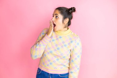 Genç ve güzel bir kadın pembe arka plan üzerine günlük süveter giyip ağızlarını eliyle kapatıyor, şok geçiriyor ve hata yapmaktan korkuyor. şaşırmış ifade