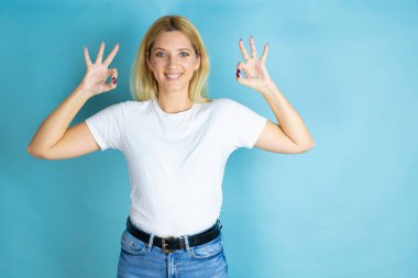 İzole edilmiş mavi arka plan üzerine gündelik tişört giyen genç ve güzel bir kadın elleriyle bana 