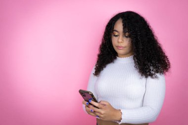 Pembe arka plan üzerine gündelik kazak giyen Afro-Amerikalı kadın telefonda sohbet ediyor.