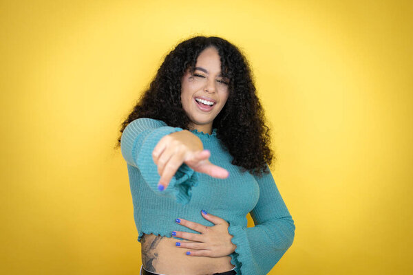 African american woman wearing casual sweater over yellow background laughing at you, pointing finger to the camera with hand over body, shame expression
