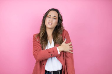 İzole edilmiş pembe arka planda, omuzlarında ağrı ve acı dolu bir ifadeyle gündelik ceket giyen genç ve güzel bir kadın.