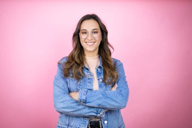 İzole edilmiş pembe arka planda kot ceket giyen genç ve güzel bir kadın mutlu bir yüzle ayakta duruyor ve gülümsüyor dişlerini gösteren bir gülümsemeyle.