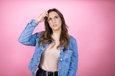 Soyutlanmış pembe arka planda kot ceket giyen genç ve güzel bir kadın soru sormayı merak ediyor. Şüpheyle karışık, kafa kafaya düşünerek.