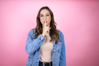 Soyutlanmış pembe arka planda kot ceket giyen genç ve güzel bir kadın sessiz olmak istiyor. Sessizlik ve gizli konsept.