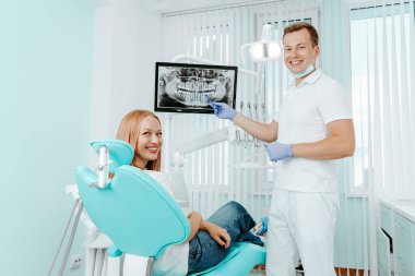 Doktor dişçi ve hasta dişçi kliniğinde gülümsüyor. Tıbbi ekipmanlarla birlikte stomatoloji kliniğindeki dijital ekranda röntgen. Gülümse sağlıklı diş konsepti