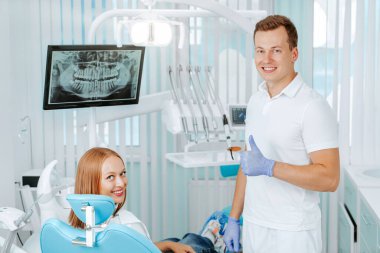 Doktor dişçi ve genç kadın hasta diş kliniğinde tıbbi malzemelerle, diş röntgeniyle, aletlerle gülümsüyorlar. Gülümse sağlıklı diş konsepti