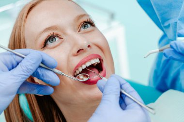 Diş kliniğinde doğal beyaz dişleriyle gülümseyen çekici genç bir kadın. Tıbbi aletlerle el doktoru diş hekimi. Sağlıklı diş konsepti