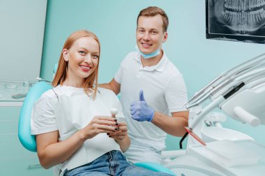 Doktor dişçi ve genç kadın hasta diş kliniğinde tıbbi malzemelerle, diş röntgeniyle, aletlerle gülümsüyorlar. Gülümse sağlıklı diş konsepti