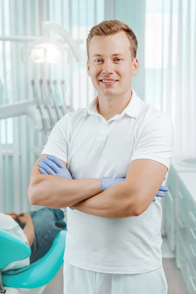 Läkare Tandläkare Ler Och Står Med Händerna Korsade Tandvårdskliniken Bakgrund — Stockfoto