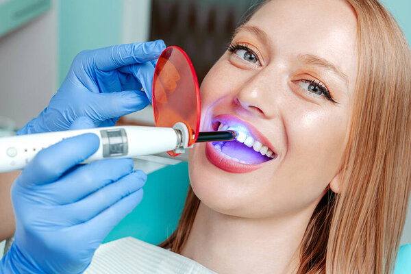 Doctor dentist whiten teeth to young attractive patient woman in stomotology clinic. Hands doctor dentist with medical tools. Healthy teeth concept