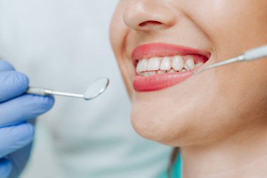 Dişçi kliniğinde açık mavi arka planda doğal beyaz dişleri olan gülümseyen bir kadın. Tıbbi aletlerle el doktoru diş hekimi. Sağlıklı diş konsepti