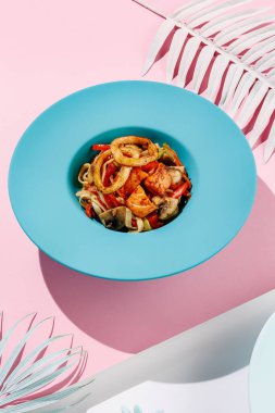 Udon with calamary and vegetables, seafood on blue pastel color plate at white background with sunlight and shadows, minimalism, squid.