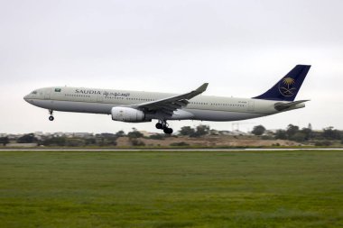 Luqa, Malta - January 19, 2023: Saudia - Saudi Arabian Airlines Airbus A330-343 (REG: HZ-AQ25) arriving in light rain for servicing in Malta. clipart