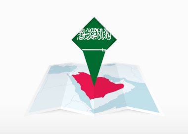 Suudi Arabistan katlanmış bir kağıt haritada resmedilmiş ve Suudi Arabistan bayrağıyla işaretlenmiş..