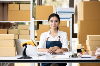 Çevrimiçi iş dünyasının ve küçük kuryenin genç bayan sahibi, ofiste oturuyor ve gururla gülümsüyor, paket teslimatı, e-ticaret.