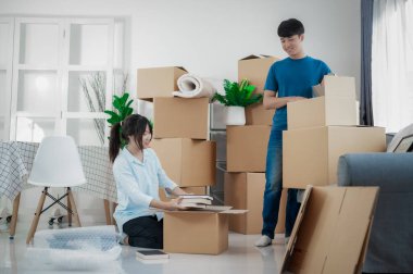 Büyük kutuları olan genç çift yeni bir eve taşınıyor, çift için yeni bir daire, genç adam ve kadın kutuları taşımaya yardım ediyorlar ve yeni ev için eşyaları düzenliyorlar, taşınıyorlar..