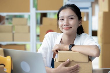 Çevrimiçi satış işleriyle uğraşan güzel genç bir kadın. Paket kutularıyla gülümseyen mutlu bir şekilde kameraya bakan, başarıyla gurur duyan genç bir iş kadını. Paket teslimatı yapan genç bir kadın..