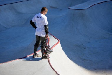 Koç yarışma için yer arıyor. Beyaz tişörtlü ve kot pantolonlu genç adam paten parkına eğitim için geldi. Spor anlayışı, hobiler, aktif yaşam tarzı. Sporcu biraz dinlensin.