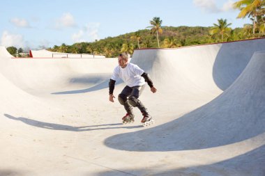 Halka açık kaykay parkında yetişkin erkek paten eğitimi. Adam zıplama, numaralar yapıyor. Aktif yaşam tarzı, spor, hareket, hobiler. Sonbahar güneşli bir günde dışarıda boş zaman aktiviteleri.