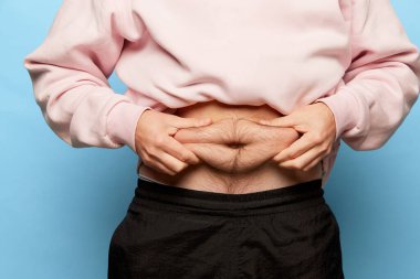 Erkek eli, karın yağlarını ölçmek için çimdik testini kullanır. Diyet, zindelik, sağlıklı beslenme kavramı. Sağlık hizmeti, vücut pozitifliği ve reklam. Kesilen resim