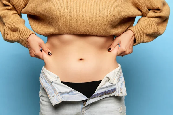 Closeup female hands stretching skin on her belly, model showing to camera her abdomen. Woman using pinch test as method for measuring body fat on belly. Concept of dieting, fitness, healthy eating