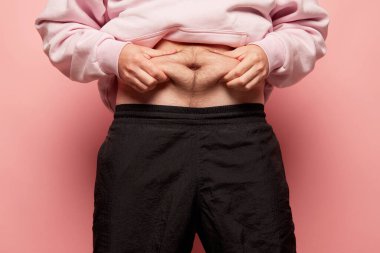 Yaklaşan erkek elleri karnının üstünde geriniyor, adam karnını kameraya gösteriyor. Diyet, spor, spor, sağlıklı yaşam tarzı, vücut pozitifliği ve refah kavramı. Liposuction ve plastik cerrahi