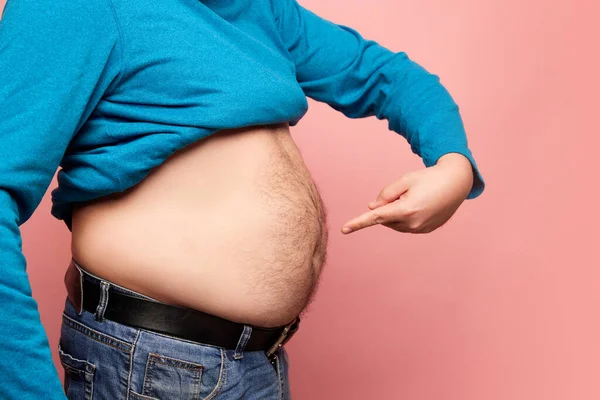 Side view. Cropped image of fat man showing his belly, abdomen isolated over pink background. Close up part of mans body. Concept of dieting, sport, fitness, body positive. Liposuction and plastic