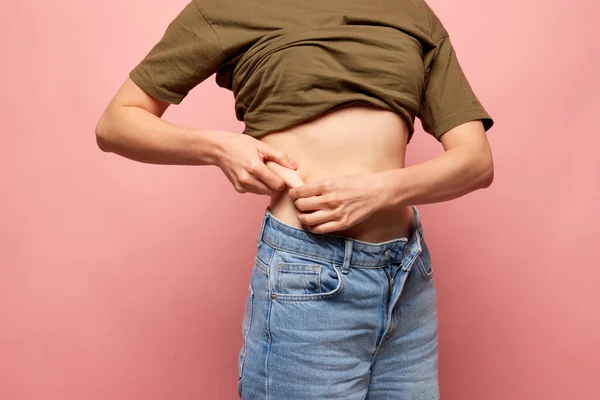 Closeup female hands stretching skin on her belly, model showing to camera her abdomen. Woman using pinch test as method for measuring body fat on belly. Concept of dieting, fitness, healthy eating