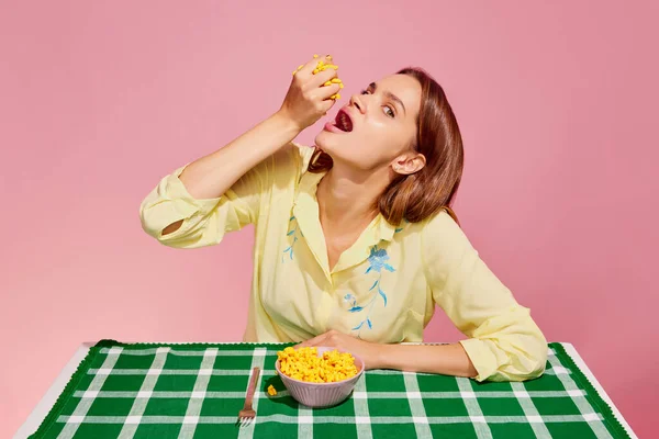 健康饮食 食品流行艺术摄影 小女孩尝着甜玉米罐头 从粉色背景中分离出来 艺术的概念 创造力 复古80年代 70年代风格 互补的颜色 广告的复制空间 — 图库照片